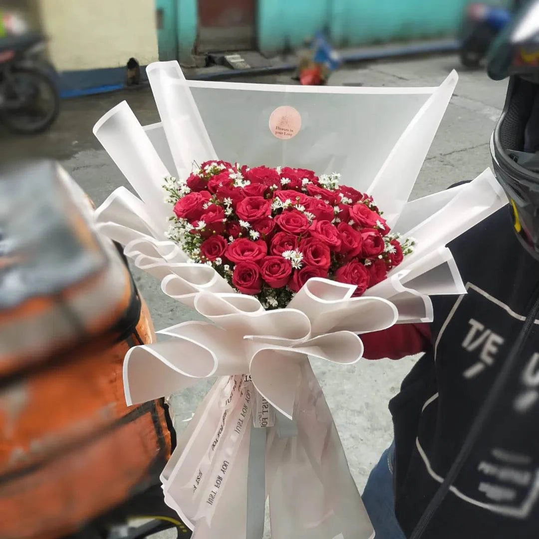 The Flowercart's Scarlet bouquet features 50 vibrant red roses with delicate baby's breath, elegantly wrapped in white paper.