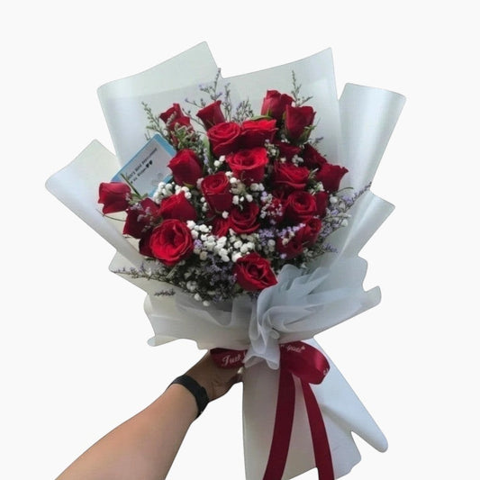 The Flowercart's Fallin For You bouquet: 24 vibrant red roses with baby's breath and misty blue fillers, elegantly wrapped.