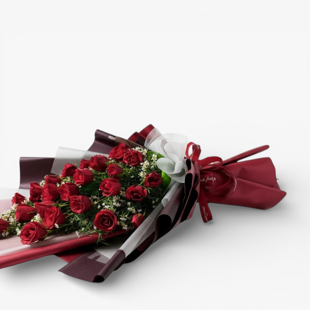 The Flowercart's Crimson Whisper bouquet: 24 red roses with white filler flowers, wrapped in burgundy and white paper, tied with a red ribbon and gold heart accents.