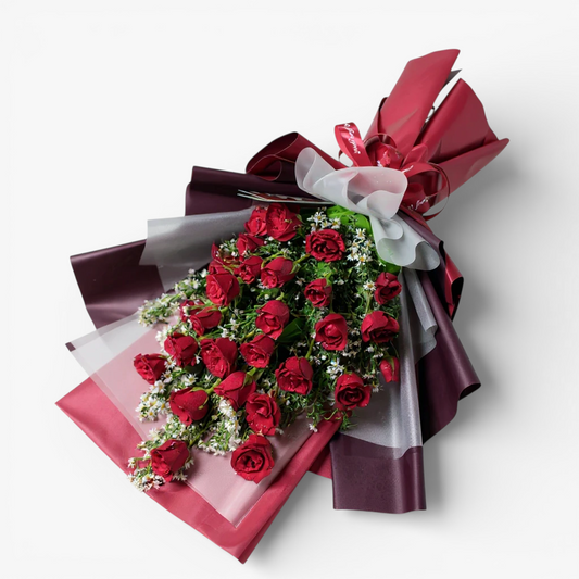 The Flowercart's Crimson Whisper bouquet: 24 red roses with white filler flowers, red ribbon, and gold heart accents.