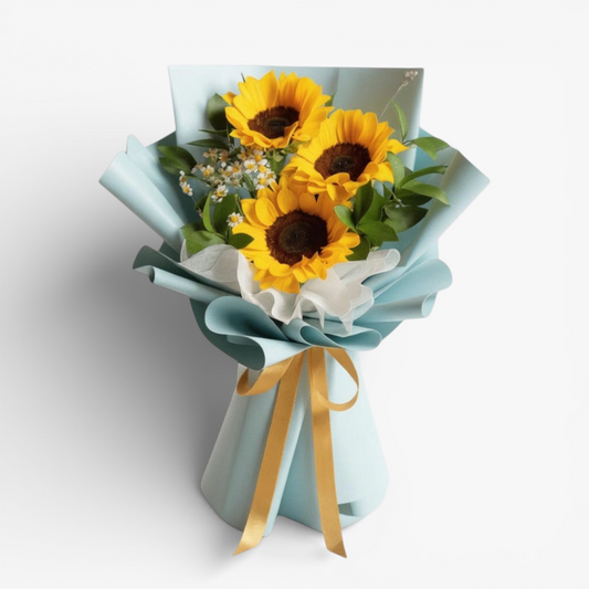 The Flowercart Sunshine Delight bouquet with three large sunflowers, white filler flowers, and green leaves, wrapped in light blue paper and tied with a gold ribbon.