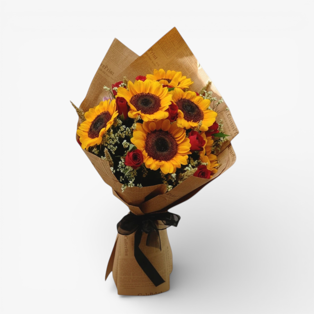 The Flowercart Sunny Blooms bouquet features 6 golden sunflowers, 12 red roses, and baby's breath, wrapped in brown paper with a black ribbon.
