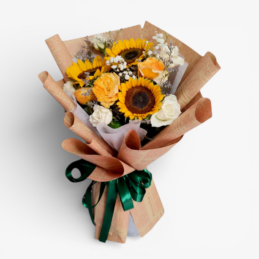 The Flowercart Sunny Serenade bouquet features sunflowers, white and yellow roses, baby's breath, and misty blue fillers, wrapped in brown paper and tied with a green ribbon.