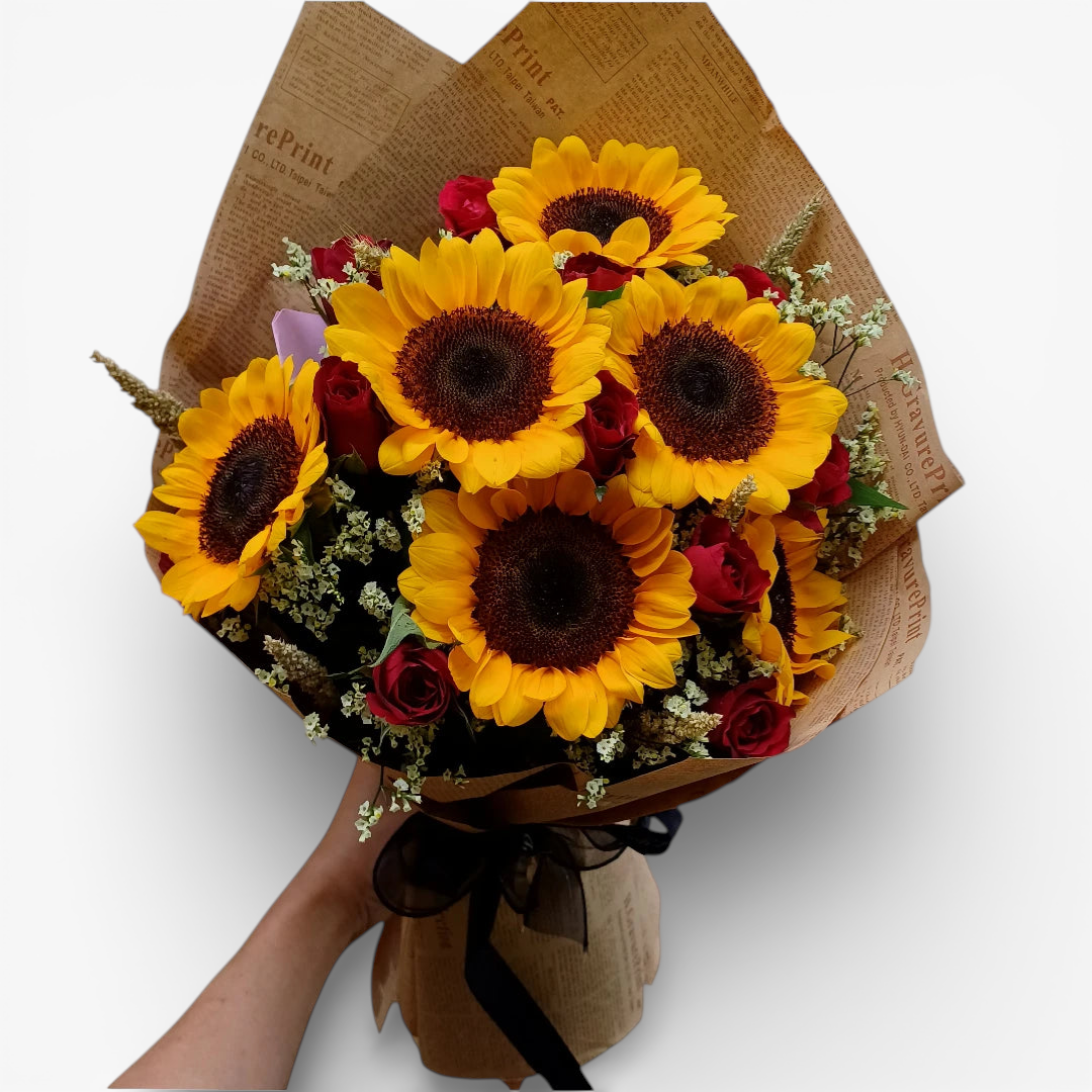 The Flowercart's Sunny Blooms bouquet features 6 golden sunflowers and 12 red roses with baby's breath, wrapped in brown paper.