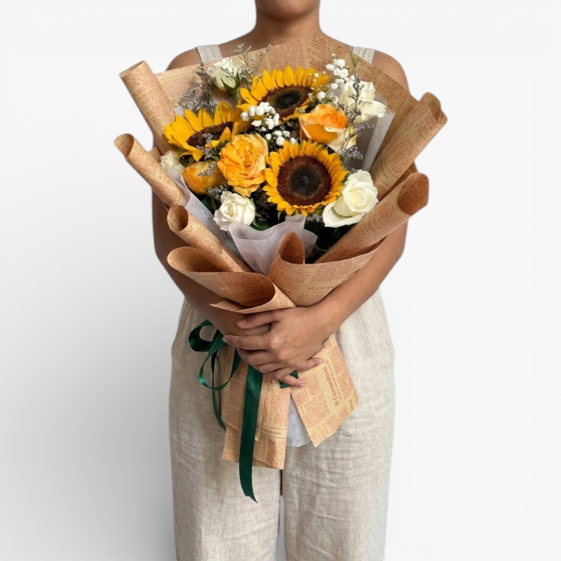 The Flowercart Sunny Serenade bouquet: sunflowers, yellow and white roses, baby's breath, and misty blue fillers in brown paper wrap.