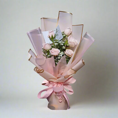 Bouquet of pink roses wrapped in pink paper with gold accents on a light gray background