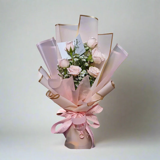 Bouquet of pink roses wrapped in pink paper with gold accents on a light gray background